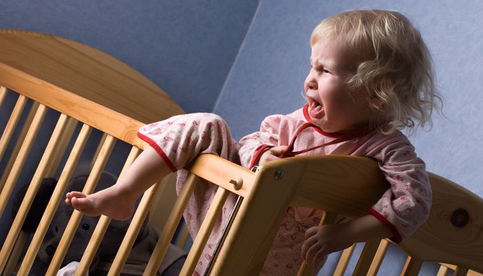 Crying baby climbing out of crib.