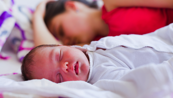 Mom napping with her baby in the same bed.