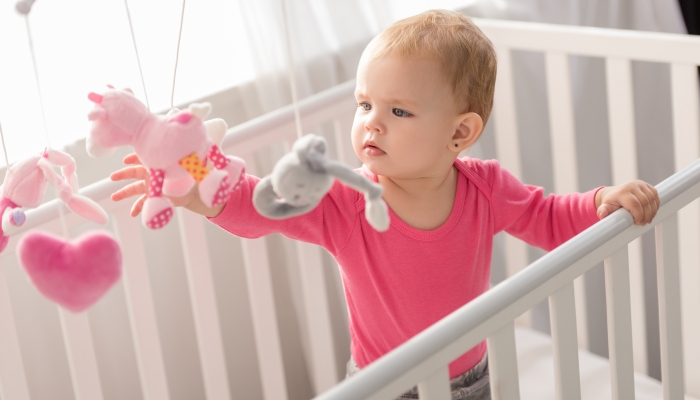 Adorable child in pink shirt standing in crib
