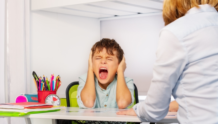 Boy screaming and closing ears in pain during development therapy.