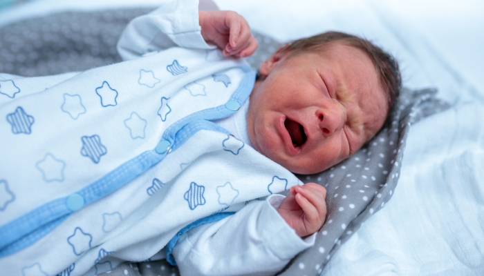 Close-up of a few days old newborn baby lying in a bed and crying.