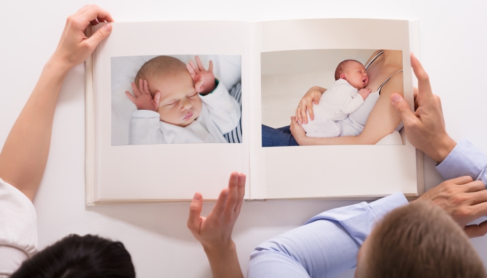 Elevated View Of Couple Looking At Baby's Photo Album On White Background