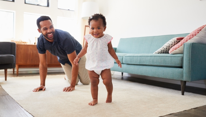 Father Encouraging Baby Daughter To Take First Steps At Home