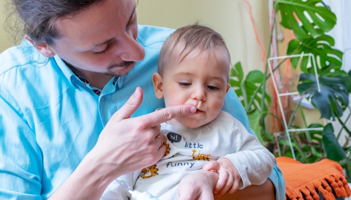 Father rubbing pain relieving gel into his little baby boy's growing teeth or gums