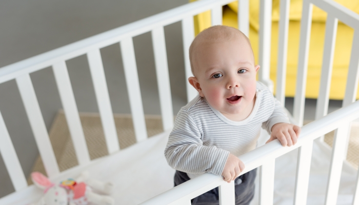 Happy little boy standing in baby crib