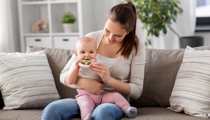 Happy smiling mother and little baby playing with teething toy or rattle at home