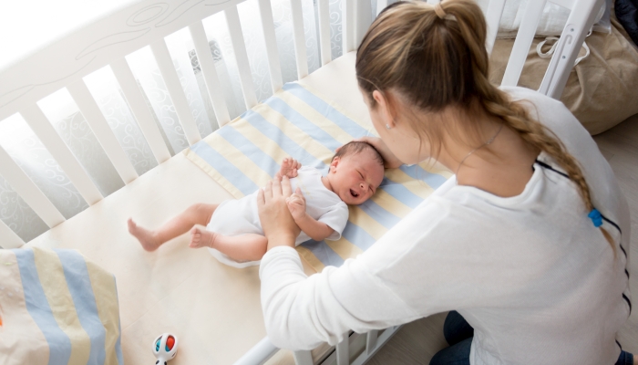 Mother sitting near the crib and holding baby's hand