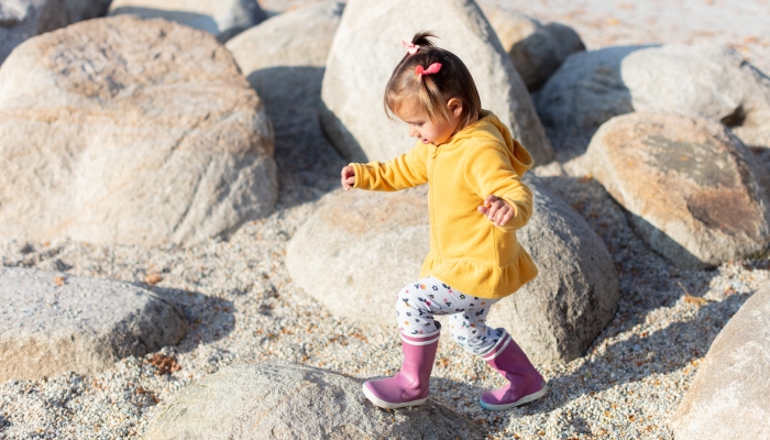 Two years old girl developing her gross motor skills by walking on big rock stones.