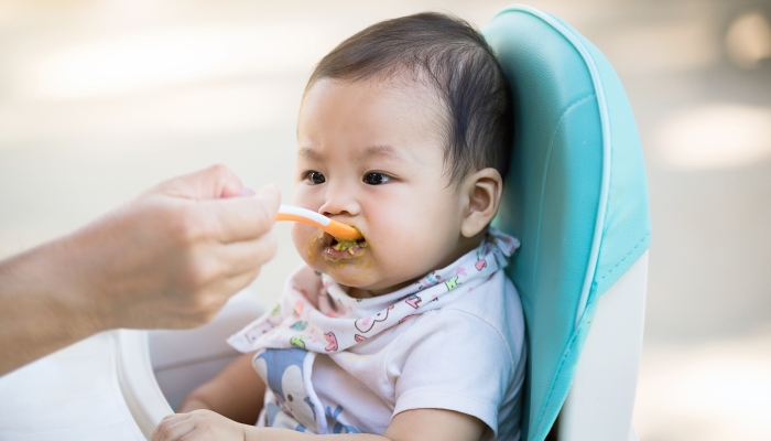 A baby girl sitting on a baby chair and eating food outdoor.