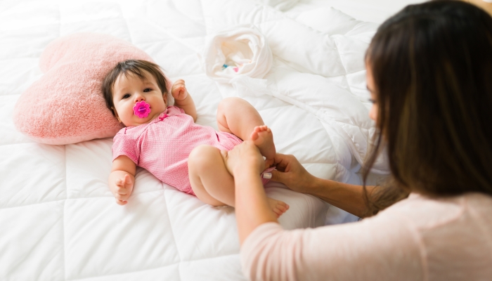 Adorable newborn baby using a pacifier and wearing a pink onesie.