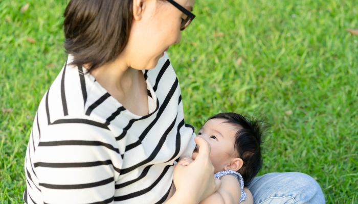 Asian mother is breastfeeding baby girl on the grass field.