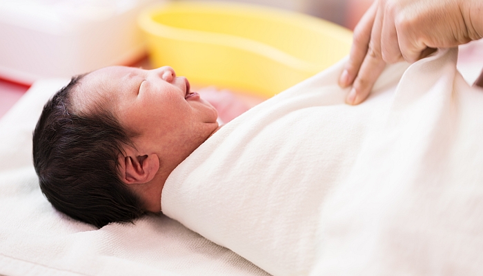 Asian new born baby smiling while mother's hand swaddling her body with white blanket.