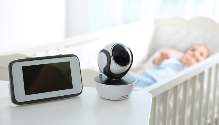 Baby monitor and camera on table near crib with child in room.