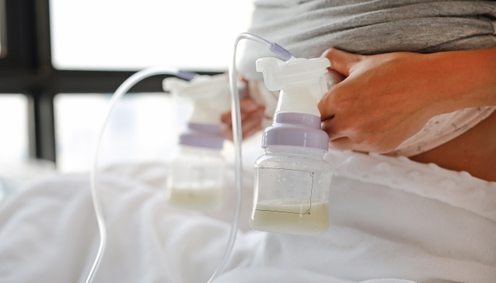 Close-up mother using automatic breast pump on the bed.