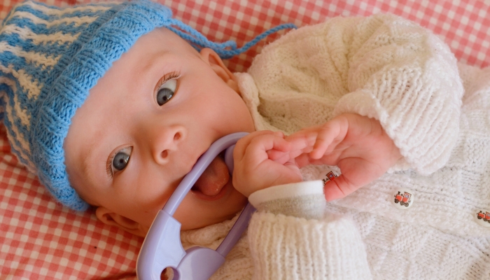 Cute baby in knitted hat and sweater playing with a rattle.