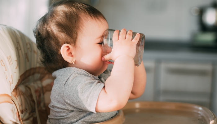 Cute little girl sitting in baby chair and drinking water.