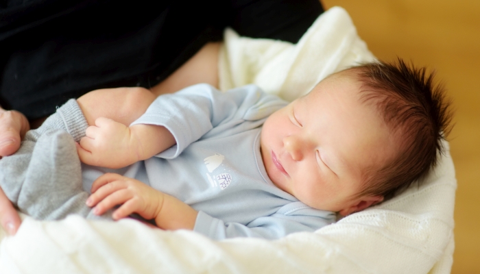 Cute little newborn baby boy sleeping in his mothers arms.