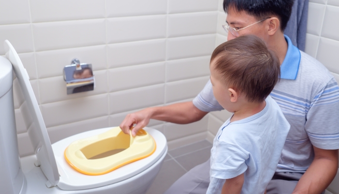 Father Training sleepy son to use toilet in bathroom.