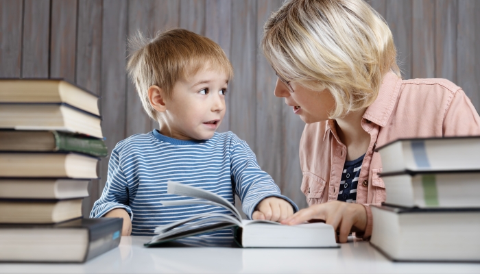 Five years old child reading a book at home with mother.