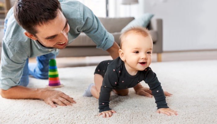 Happy little baby girl with father at home crawling on floor.