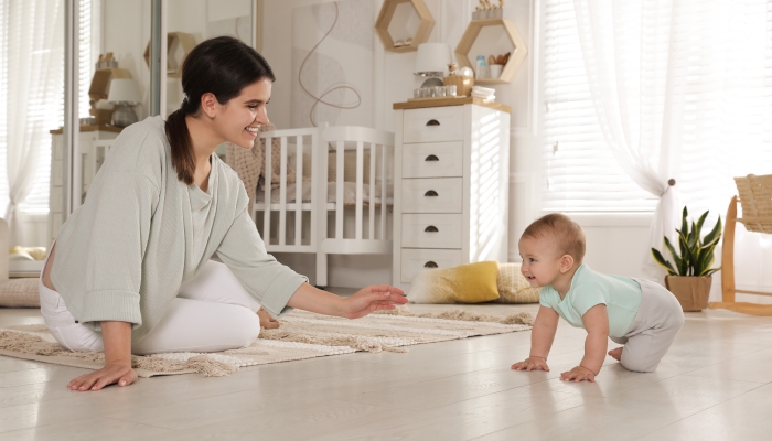 Happy young mother watching her cute baby crawl on floor at home.