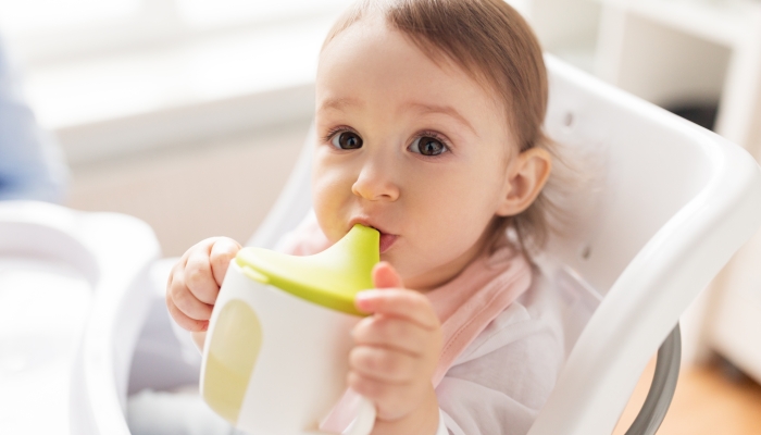 Little baby drinking from spout cup sitting in highchair at home.