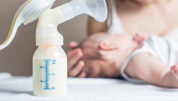 Manual breast pump with milk, mother and baby at background.