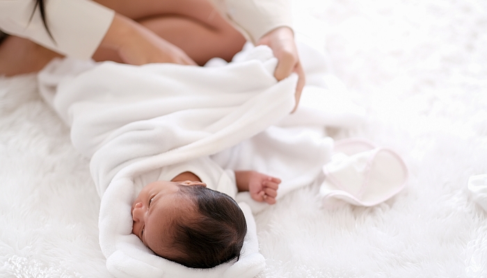 Newborn baby was swaddling with white cloth by her mother.