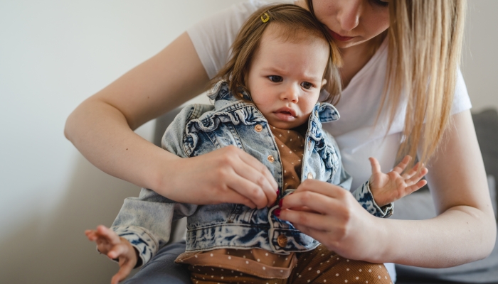 Small caucasian baby girl infant child with her mother dressing or undressing small daughter at home.