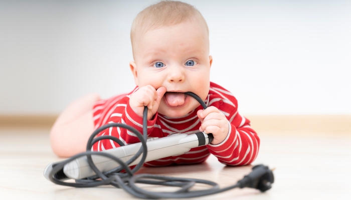 Small child playing and chewing with electrical wire of a curling iron on floor at home.