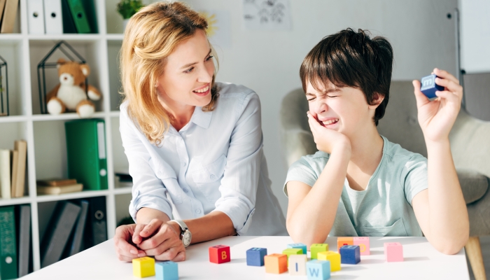 Smiling child psychologist and kid with dyslexia playing with building blocks.