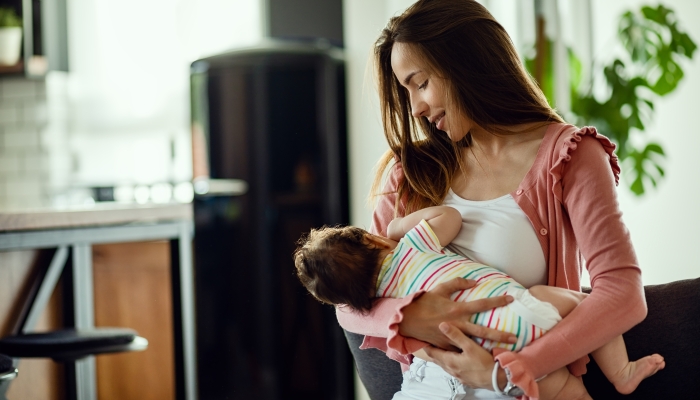 Smiling mother breastfeeding her baby daughter while being at home.