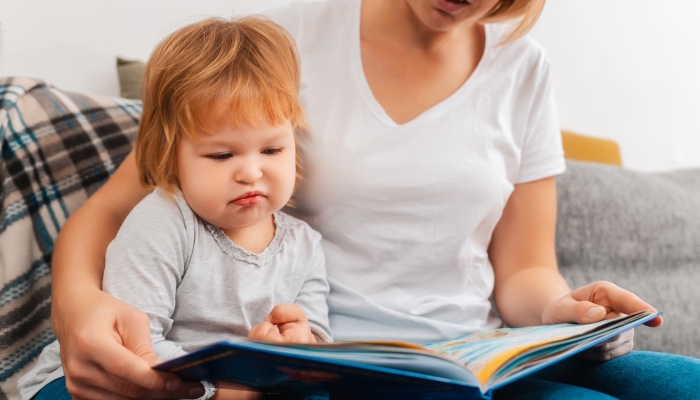 Speech therapist is reading a book to bored child sitting on the sofa.