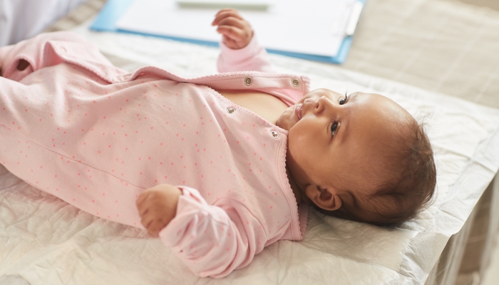Warm-toned portrait of cute baby girl lying on changing table at doctors office in pink onesie.