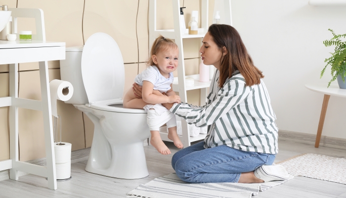 Woman teaching her baby to use toilet bowl in bathroom.
