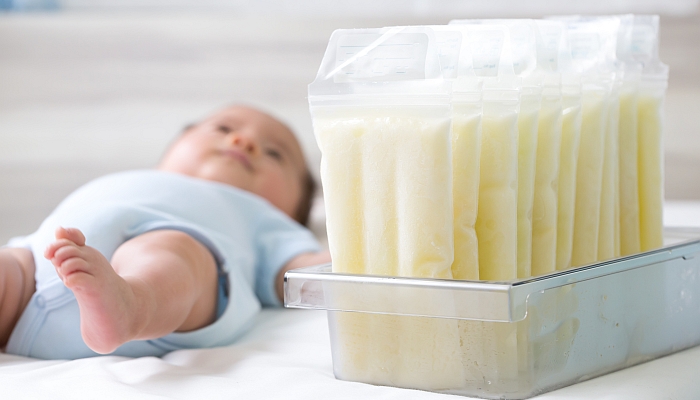 Breast milk frozen in storage bag and baby lying on background.