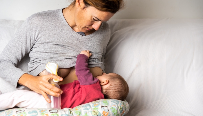 Busy mother breastfeeding her newborn baby while using an manual.