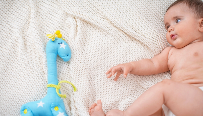 Cute chubby baby 4 months old is lying on his side on bed with toy.