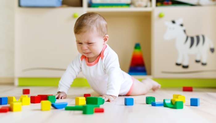 Cute sad crying baby playing with colorful wooden blocks toys.