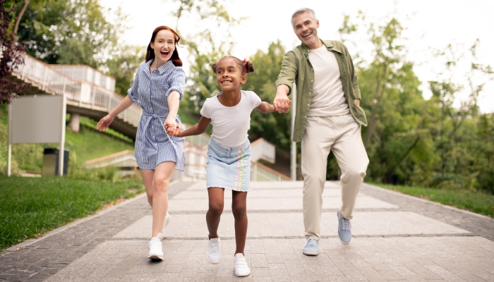 Funny African-American daughter running while walking with parents in the park