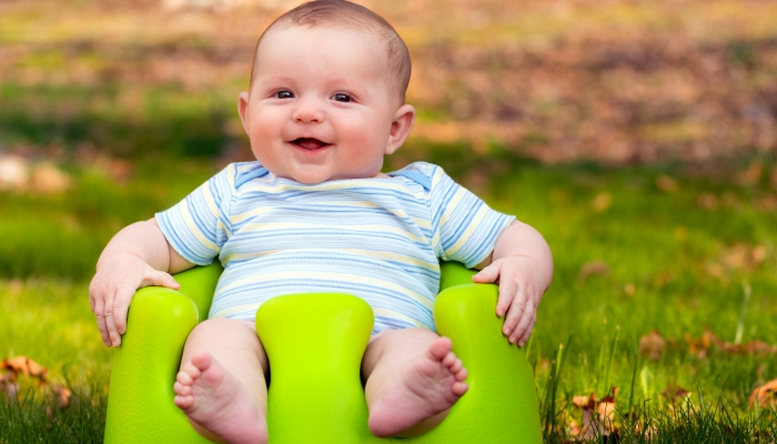 Happy infant baby boy using training Bumbo seat to sit up.