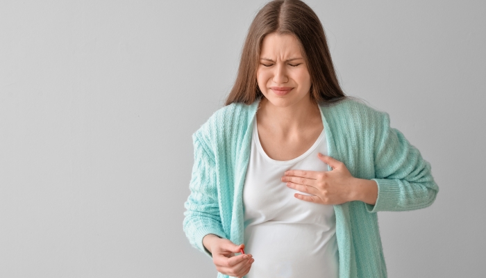 Ill pregnant young woman with pill on grey background.