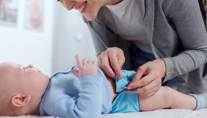 Mom changes a reusable diaper to a baby on a changing table.