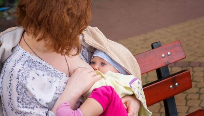 Mother breastfeeding baby on a bench in the Park.