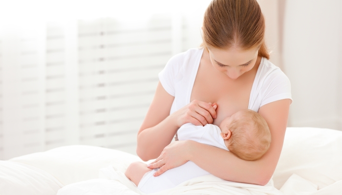 Mother breastfeeding newborn baby in white bed.