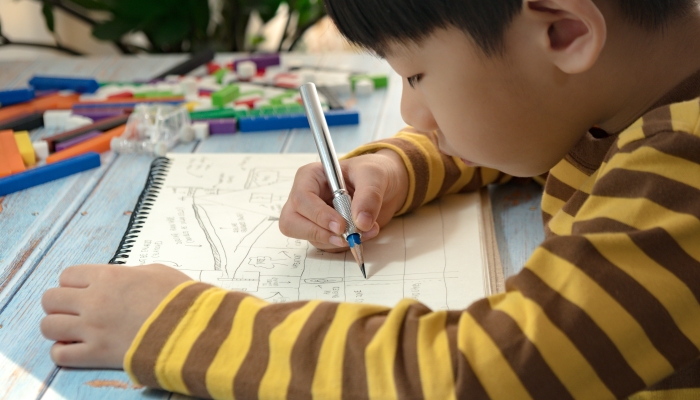 Smart asian little boy sitting on his table concentrating on his drawing.