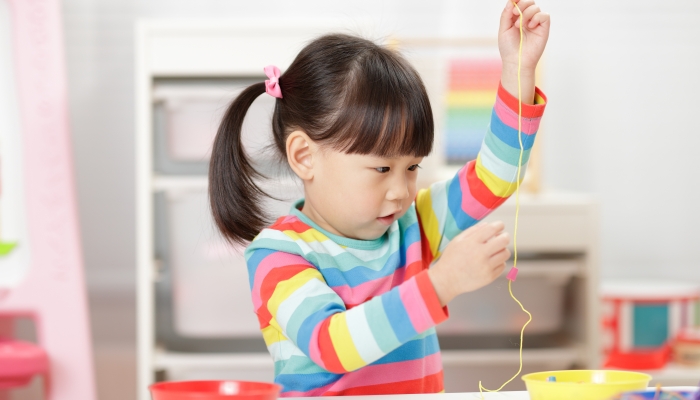 Young girl string wooden bead craft for homeschooling.