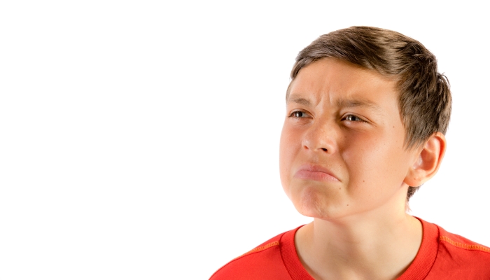 Young teenage boy isolated on a white background wrinkling his nose.