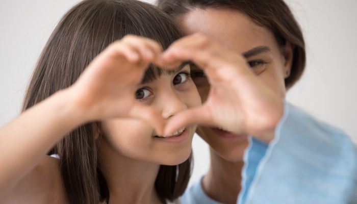 Mother and daughter making heart symbol with hands.