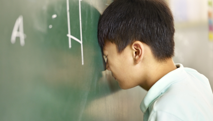 Asian elementary schoolboy banging his head on blackboard.